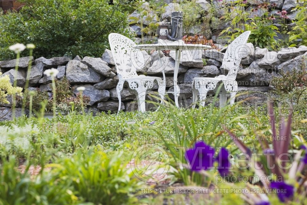 White cast iron metal Victorian sitting chairs and round table next to raised stone borders  